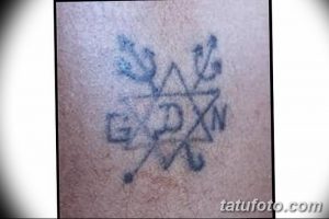Фото старой татуировки: Звезда Давида с окружающими ее надписями на неизвестном языке, выполненная в синих тонах. Винтажный стиль.