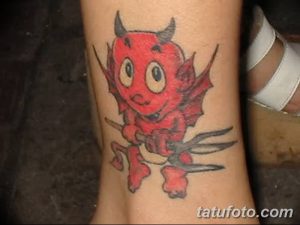 Фото тату маленького дьяволенка с трезубцем на лодыжке. Цветная татуировка в мультяшном стиле с яркими красками.
