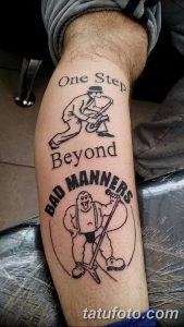 Фото тату на руке: мультяшный герой с надписью "One Step Beyond Bad Manners". Стиль мультфильм, яркие цвета, юмористический сюжет.