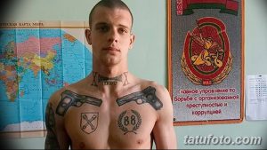 Фото тату на груди мужчины: два пистолета, кресты и надписи в криминальном стиле. Детализированный рисунок татуировки.