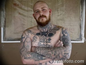 Фото тату с множеством символов и портретов в стиле skinhead на теле мужчины. Черно-серый рисунок татуировки.