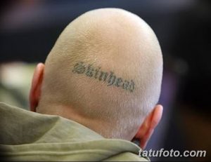 Фото тату надписи 'skinhead' на бритой голове мужчины. Черно-серый рисунок татуировки выполнен простым шрифтом.