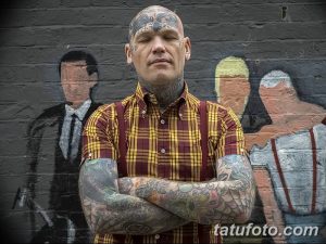 Фото мужчины с многочисленными татуировками на лице, шее и руках в стиле Skinhead. Экстремальный и противоречивый образ.