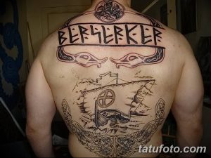 Фото татуировки в стиле викингов на спине, изображающей корабль, руны и волчьи головы. Детализированный рисунок татуировки.