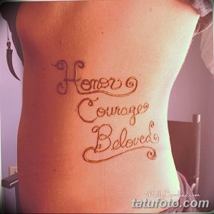 Фото тату мехенди на спине с надписью "Honor Courage Beloved" в красивом каллиграфическом стиле. Коричневые оттенки и изящные завитки.