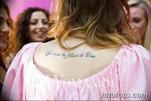 Фотография девушки с татуировкой надписью на спине. Изображение сделано сзади, акцент на татуировке и плечах.