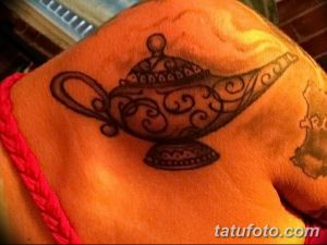 Фото татуировки в стиле blackwork на плече с изображением лампы Аладдина. Черные линии, геометрические узоры и минималистичный дизайн.