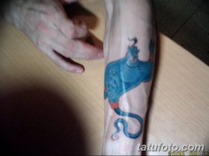 Фото тату Джинна из Аладдина на предплечье. Яркий синий цвет, мультяшный стиль, детализированный рисунок татуировки.