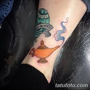 Фото тату на предплечье: яркая лампада Алладина, свиток с надписью и дым, выполненные в мультяшном стиле. Идеи для тату.