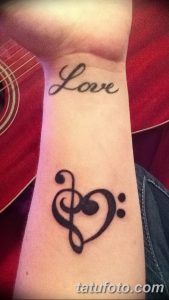 Фото тату с надписью 'Love' и музыкальным ключом в форме сердца на запястье. Черно-белый рисунок татуировки для меломанов.