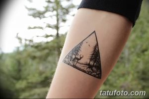 Фото тату леса в треугольнике на руке. Черно-белый рисунок татуировки изображает деревья, оленей и птиц внутри геометрической фигуры.