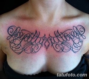 Фото татуировки с надписью "Loyalty Loyalty" выполненной красивым шрифтом с декоративными элементами на женской груди. Черно-белый рисунок.