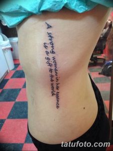 Фото тату: черная надпись на боку, гласящая 'A strong woman in her essence is a gift to the world'. Простой, но вдохновляющий рисунок татуировки.