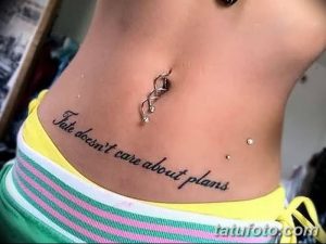 Фото тату надписи 'Fate doesn't care about plans' на животе. Минималистичная татуировка, выполненная черным цветом, с изящным шрифтом.