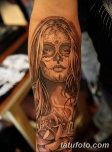 Фото тату: реалистичная татуировка в стиле сахарной черепушки (Santa Muerte) на предплечье женщины, выполненная в черно-серых тонах с детальной проработкой.