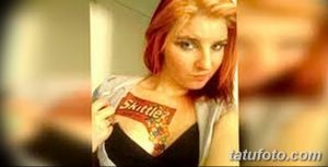 Фото тату: яркая и необычная татуировка с логотипом Skittles и разноцветными конфетами на груди девушки.