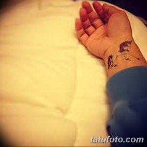 Фото тату на руке с изображением одуванчика, из которого разлетаются семена. Черно-белый рисунок в минималистичном стиле.