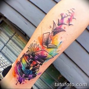 Фото тату на предплечье с изображением стопки книг, из которых вылетают бумажные птицы. Акварельная техника, яркие цвета.