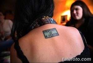 Фото тату: татуировка в виде ярлыка 'PROPERTY OF M. FENTON' на женской спине. Оригинальный и необычный рисунок татуировки.