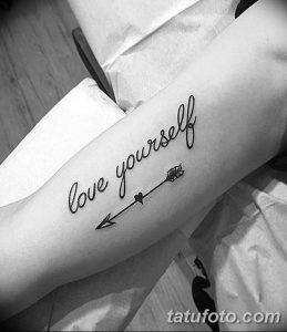 Фото тату: стильная надпись "love yourself" с изображением стрелы и сердца на предплечье. Черно-белый рисунок выглядит лаконично и вдохновляюще.