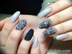 Фото маникюра: овальные ногти светло-серого цвета с черными кружевными узорами и одним черным матовым ногтем. Идеально для создания элегантного и загадочного образа.