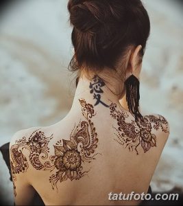 Фото тату мехенди на спине, выполненное в коричневых тонах. Детализированный рисунок с цветочными элементами, узорами и иероглифами.
