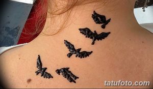 Фото тату с изображением пяти черных воронов, летящих вверх по шее. Детализированный рисунок с акцентом на крылья и перья.
