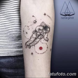 Фото тату: минималистичный рисунок космонавта в открытом космосе на руке. Тонкие линии, планеты, звезды.