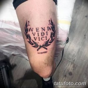 Фото татуировки на ноге с латинской фразой "Veni, Vidi, Vici" и изображением скрещенных мечей, обрамленных лавровыми венками. Минималистичный рисунок татуировки в стиле графика.