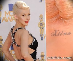 Фото тату Кристины Агилеры на лопатке: надпись 'Xtina' черным цветом, выполненная в элегантном шрифте. Крупный план демонстрирует детали татуировки.