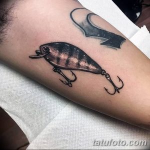 Фото реалистичной татуировки воблера с тройными крючками на руке. Детализированный рисунок для любителей рыбалки и реализма.
