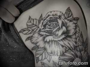 Фотография татуировки на плече, изображающей большую розу с листьями, выполненную в стиле blackwork с использованием черных линий и точек.