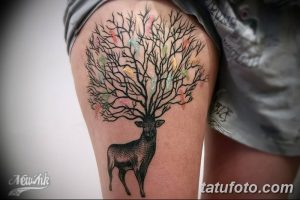 Фотография акварельной татуировки на бедре, изображающей оленя, стоящего под цветущим деревом с пастельными оттенками.