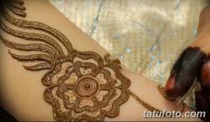 Фото процесса нанесения тату хной на руку, с изображением цветка и мастером, работающим над рисунком. Идеально для вдохновения и понимания техники.