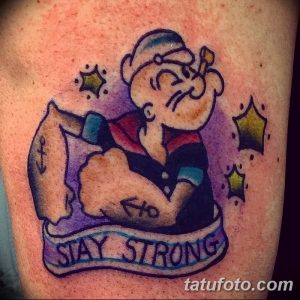 Фото тату Попая, демонстрирующего свою силу, с надписью "Stay Strong". Яркие цвета, мультяшный стиль и мотивирующая надпись.