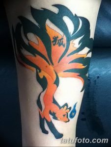 Фото татуировки девятихвостого лиса Курамы из аниме Наруто на руке. Яркие оранжевые и черные цвета, динамичная поза, аниме стиль.