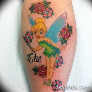 Цветная татуировка на предплечье с изображением феи Tinker Bell из мультфильма Питер Пэн, окруженной розовыми цветами. Рисунок выполнен в мультяшном стиле.