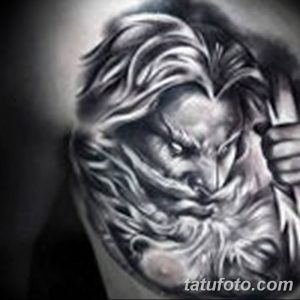 Черно-серая татуировка на руке с реалистичным портретом пожилого мужчины с длинной бородой и вьющимися волосами. Детализированный рисунок татуировки выполнен в стиле реализм.