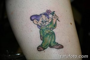 Фото тату Думпи, одного из семи гномов из сказки Белоснежка, с цветком в руке. Яркий и красочный рисунок для поклонников Disney.