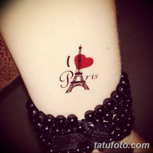 Небольшая татуировка на руке с надписью "I Love Paris" и изображением Эйфелевой башни, выполненная в красных и черных тонах.