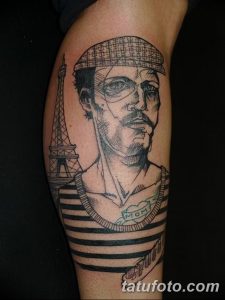 Фотография реалистичной татуировки на ноге, изображающей моряка в тельняшке с Эйфелевой башней на фоне. Черно-белый рисунок татуировки с высокой детализацией.