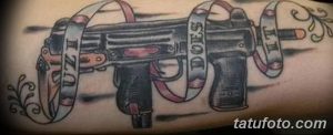 Фото тату на руке с изображением пистолета UZI и надписями 'UZI DOES IT'. Стильный и дерзкий рисунок татуировки.