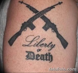 Фото тату на руке с изображением двух перекрещенных автоматов и надписью 'Liberty or Death'. Классический рисунок татуировки.