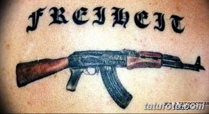Фото тату: реалистичное изображение автомата Калашникова с надписью 'FREIHEIT' (свобода) на немецком языке. Татуировка выполнена в цвете.