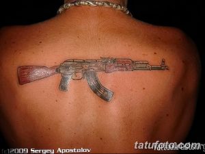 Фото тату автомата Калашникова на спине, выполненное в реалистичном стиле с использованием коричневых и серых оттенков.
