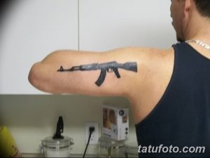 Фото тату минималистичного автомата Калашникова на руке, выполненное в черно-серых тонах с акцентом на силуэт.