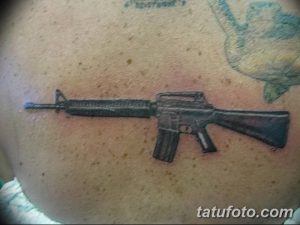 Фото тату реалистичного автомата на груди мужчины. Детализированный рисунок оружия в серо-черных тонах, выполненный опытным мастером тату.