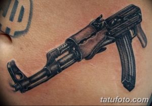 Цветная татуировка автомата Калашникова на груди. Реалистичный рисунок с детальной проработкой и использованием коричневых и черных оттенков.