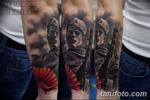 Детализированная черно-серая татуировка на руке, изображающая солдата с автоматом Калашникова и красным маком. Реалистичный портрет с множеством мелких деталей.