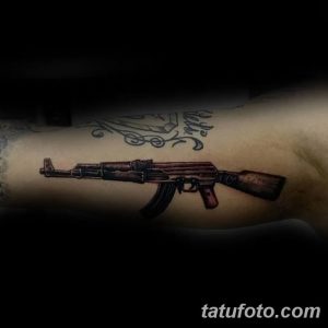 Цветная татуировка автомата Калашникова на предплечье. Реалистичный рисунок с проработкой деталей и использованием коричневых и черных оттенков.